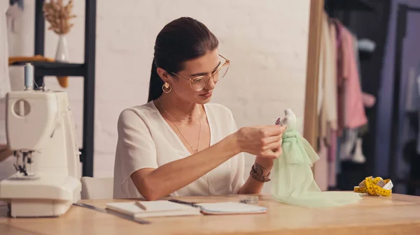 Näherin fertigt Kleid auf kleiner Schaufensterpuppe nahe verschwommener Nähmaschine im Atelier — Stockfoto