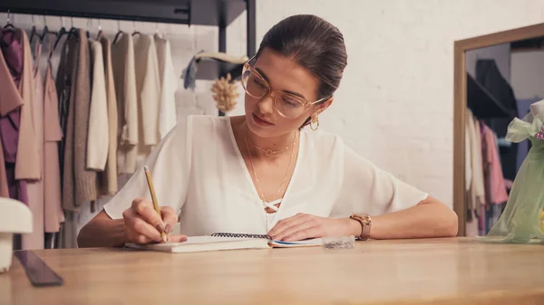 Брюнетка дизайнер в очках, пишущая на ноутбуке в ателье — стоковое фото