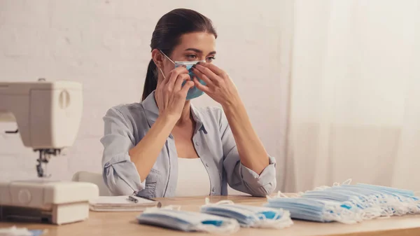 Costurera con máscara médica cerca borrosa cuaderno en el taller - foto de stock