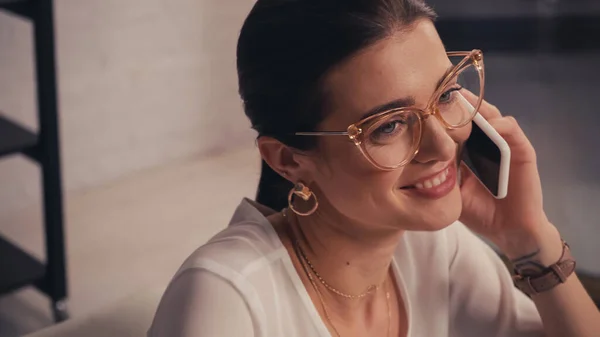 Cheerful designer in eyeglasses talking on mobile phone in atelier — Stock Photo