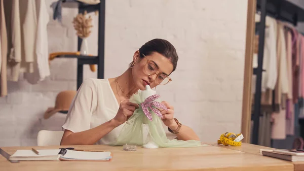 Designer fertigt Kleid auf kleine Schaufensterpuppe in der Nähe von Notizbüchern im Atelier — Stockfoto