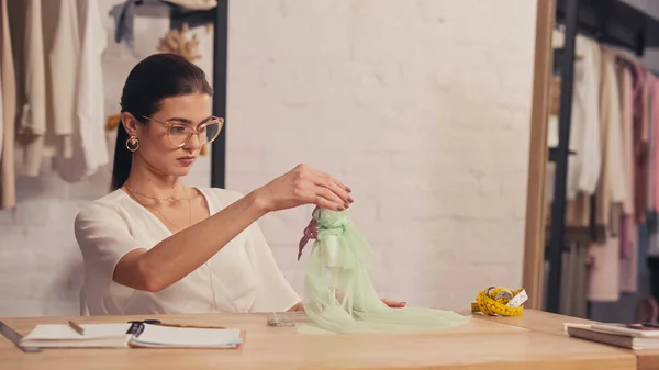 Designerin fertigt Kleid auf kleiner Schaufensterpuppe neben Maßband und verschwommenem Notizbuch im Atelier — Stockfoto