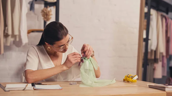 Designerin fertigt Kleid auf kleiner Schaufensterpuppe in der Nähe von Notizbüchern und Maßband im Atelier — Stockfoto