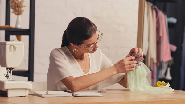 Costurera haciendo vestido en maniquí cerca del cuaderno y cinta métrica en atelier - foto de stock