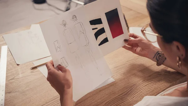 Blurred seamstress in eyeglasses holding sketches in atelier — Stock Photo