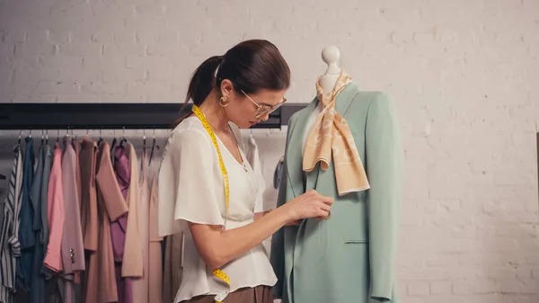 Diseñador con cinta métrica trabajando con chaqueta en maniquí en atelier - foto de stock