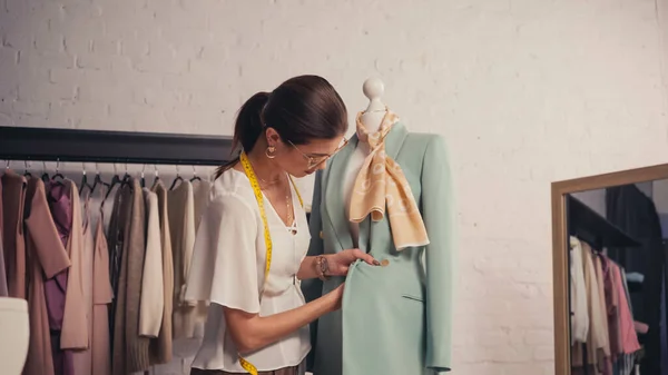 Brunette designer with tape measure working with blazer on mannequin in workshop — Stock Photo