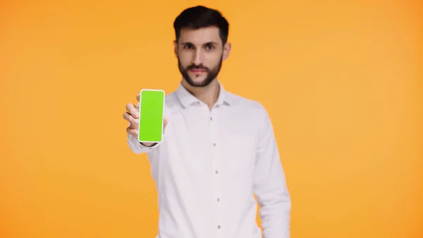 Hombre barbudo en camisa blanca sosteniendo teléfono inteligente con pantalla verde aislado en amarillo - foto de stock