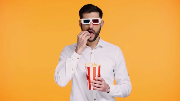 Hombre barbudo en gafas 3d sosteniendo cubo rayado y comer palomitas de maíz aislado en amarillo - foto de stock