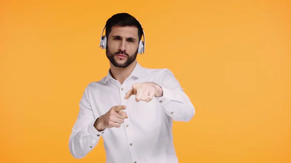 Bearded man in wireless headphones pointing with fingers and looking at camera isolated on yellow — Stock Photo