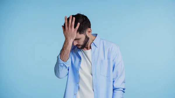Homem barbudo descontente na camisa tocando a cabeça com a mão isolada no azul — Fotografia de Stock