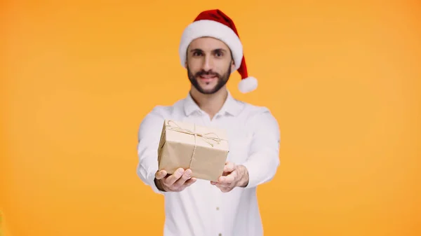 Barbudo hombre en rojo santa sombrero dando regalo de Navidad aislado en amarillo - foto de stock