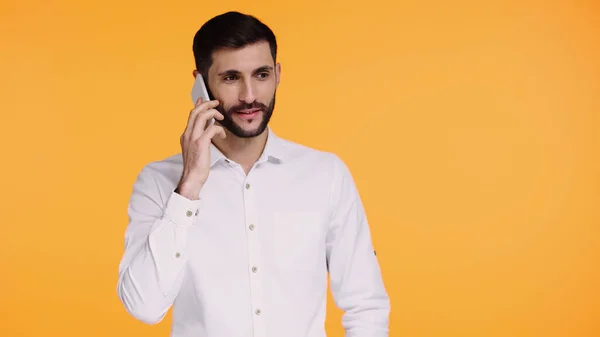 Homem barbudo em camisa branca falando no smartphone isolado no amarelo — Fotografia de Stock