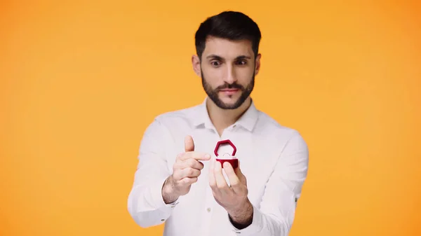 Uomo barbuto in camicia bianca che punta alla scatola con anello di fidanzamento mentre fa proposta isolata sul giallo — Foto stock