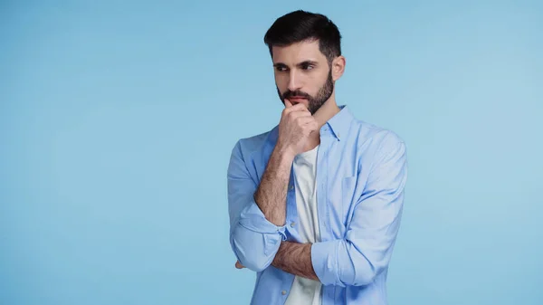 Hombre pensativo en camisa tocando la barba mientras piensa aislado en azul - foto de stock