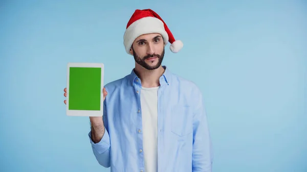 Barbu homme en rouge santa chapeau tenant tablette numérique avec écran vert isolé sur bleu — Photo de stock