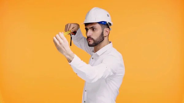Ingeniero enfocado en casco de seguridad mirando cinta métrica aislada en amarillo - foto de stock