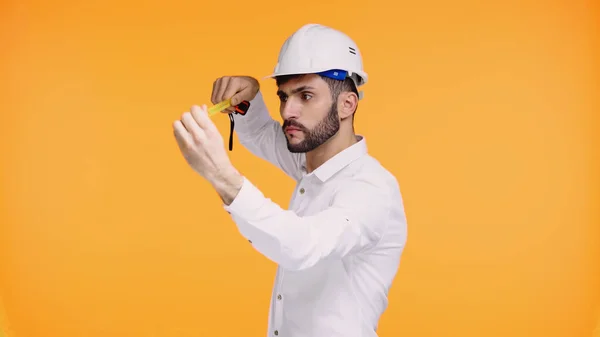 Ingénieur concentré dans le casque de sécurité regardant ruban de mesure isolé sur jaune — Photo de stock