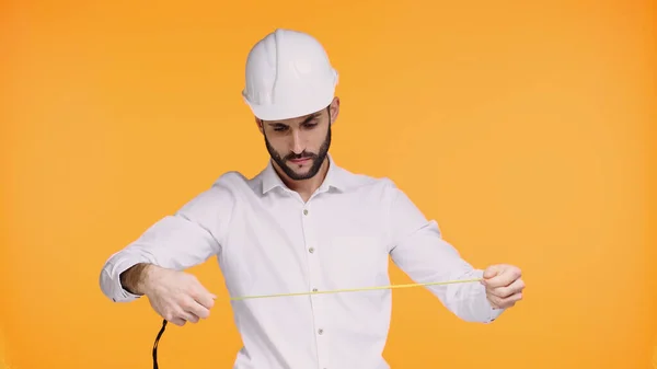 Ingénieur concentré en casque dur regardant ruban de mesure isolé sur jaune — Photo de stock