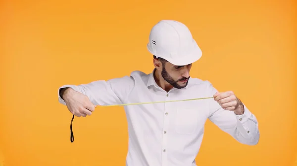 Focused architect in hard hat looking at measuring tape isolated on yellow — Stock Photo