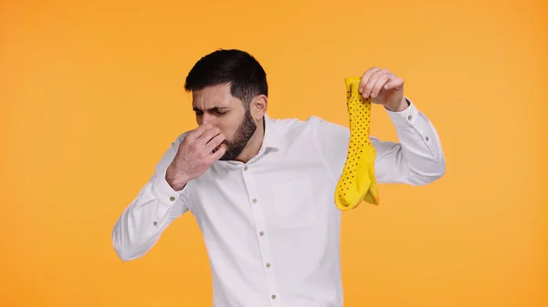 Displeased man in white shirt holding stinky socks while plugging nose isolated on yellow — Stock Photo