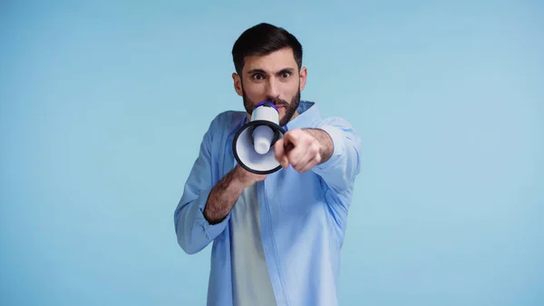 Emotional man making announcement in loudspeaker and pointing with finger isolated on blue — Stock Photo