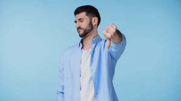 Disappointed man with closed eyes showing thumb down isolated on blue — Stock Photo