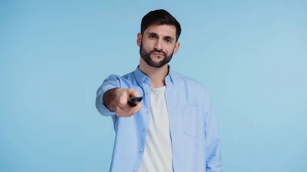 Bearded man in shirt looking at camera while clicking channels isolated on blue — Stock Photo