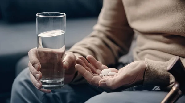 Cropped view of senior man with dementia holding pills and glass of water — Stock Photo