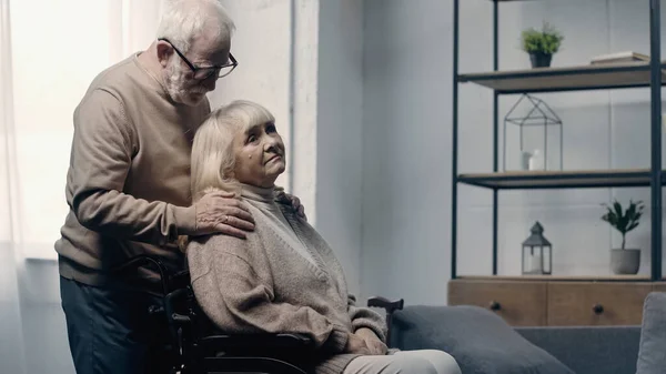 Старший мужчина успокаивает жену-инвалида слабоумием в инвалидном кресле — стоковое фото