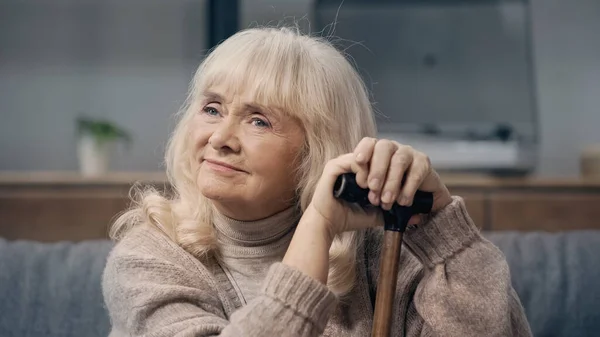 Smiling senior woman with dementia sitting with walking cane and looking away — Stock Photo