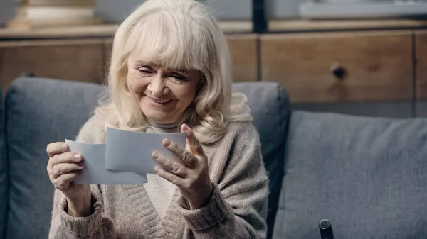 Happy senior woman with dementia holding printed photographs at home — Stock Photo