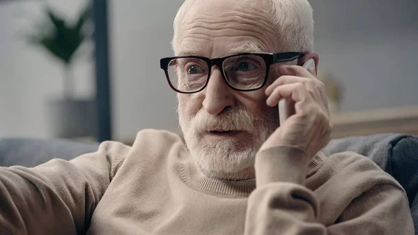 Bearded senior man in eyeglasses talking on mobile phone at home — Stock Photo