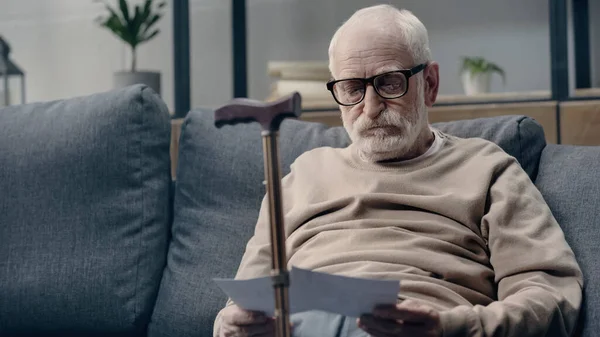 Senior man with dementia looking at photos near walking cane — Stock Photo