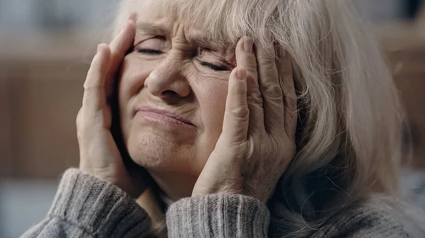 Mulher idosa com olhos fechados que sofre de enxaqueca e cabeça comovente — Fotografia de Stock