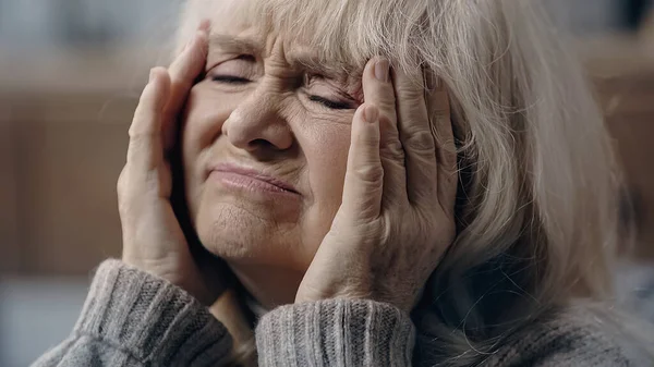 Senior woman with closed eyes suffering from migraine and touching head — Stock Photo