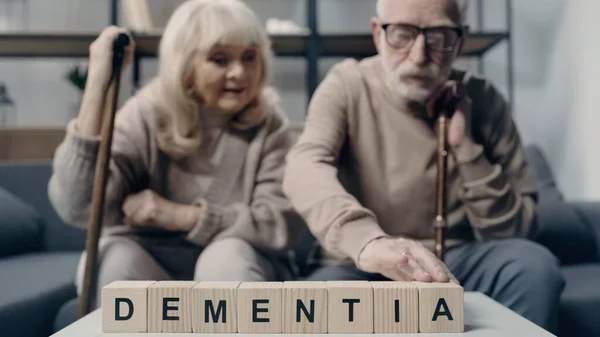 Senior woman sitting near man putting wooden cube with lettering and creating word dementia — Stock Photo