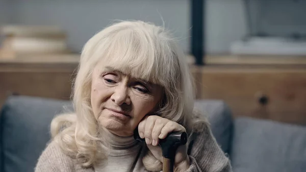 Расстроенная пожилая женщина со слабоумием сидит с тростью дома — стоковое фото