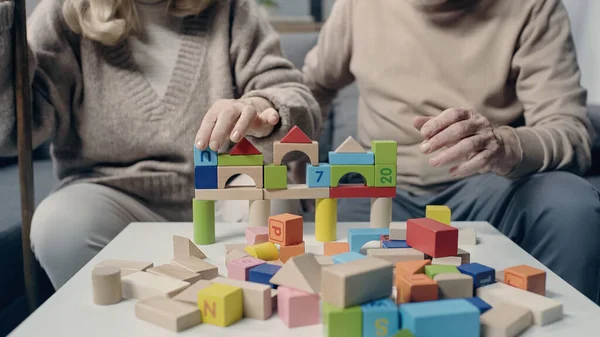 Cropped view of senior couple with dementia playing with colorful building blocks on table — Stock Photo