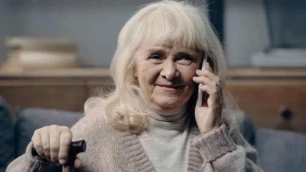 Happy senior woman with walking stick talking on smartphone — Stock Photo