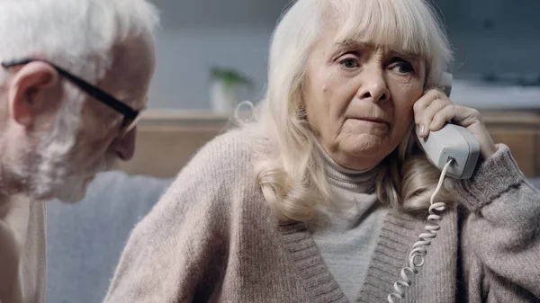 Confused senior woman with dementia talking on retro telephone near bearded husband — Stock Photo