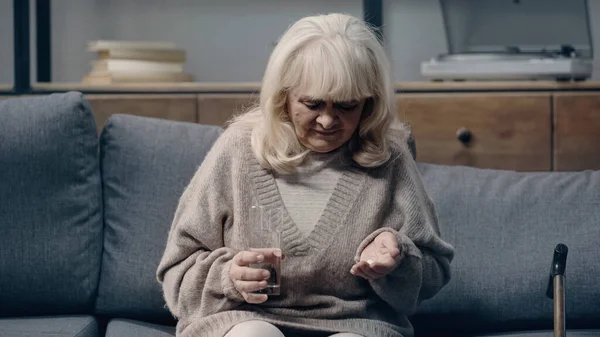 Traurige Seniorin mit Demenz hält Tabletten und Glas Wasser in der Hand — Stockfoto