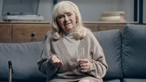 Sad senior woman with dementia holding pills and looking at camera — Stock Photo