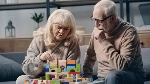 Пожилая женщина со слабоумием играет с красочными блоками рядом с мужем дома — стоковое фото