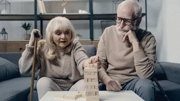 Senior woman with walking cane playing in blocks wood game near bearded husband — Stock Photo