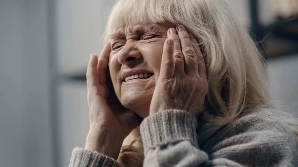 Старшая женщина с закрытыми глазами, страдающая головной болью и трогательной головой — стоковое фото