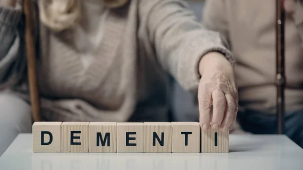 Vista recortada del hombre mayor sentado cerca de la mujer poniendo cubo de madera con letras y la creación de la demencia palabra - foto de stock