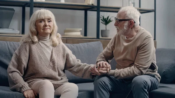 Senior man calming down uncertain wife with dementia sitting on couch — Stock Photo