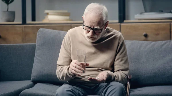 Senior man with dementia holding pills and glass of water at home — Stock Photo