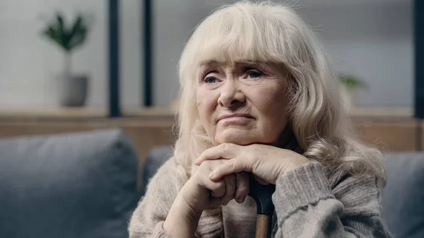 Jubilada mujer mayor con demencia sentada con bastón en casa - foto de stock
